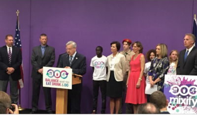 American Beverage Association. A meeting of a group of people standing around a podium with a speaker talking.