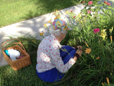 Bishop's Glen, a woman kneels in the grass along a sidewalk to do some gardening.