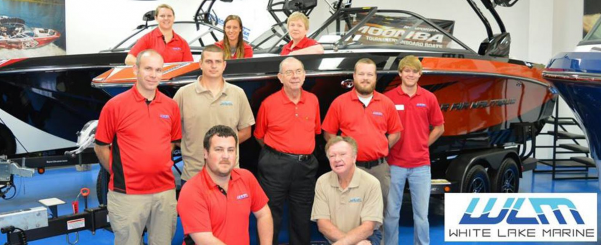White Lake Marine employees posing for a photo in their show room in front of a boat.