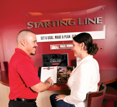 A Max Muscle employee stands next to a woman sitting at a station they have set up to get started with Max Muscle.
