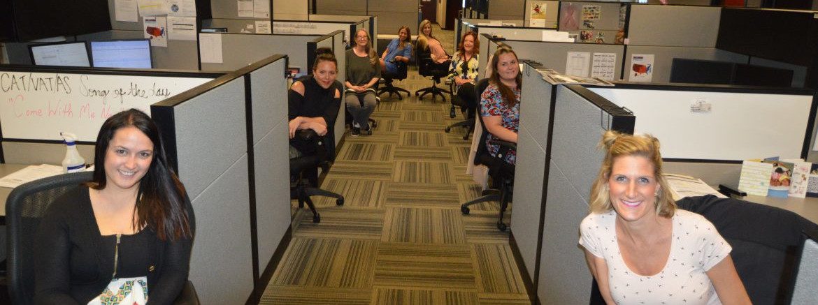 The Remi Group office photo of employees sitting and leaning outside of their cubicles for a photo.