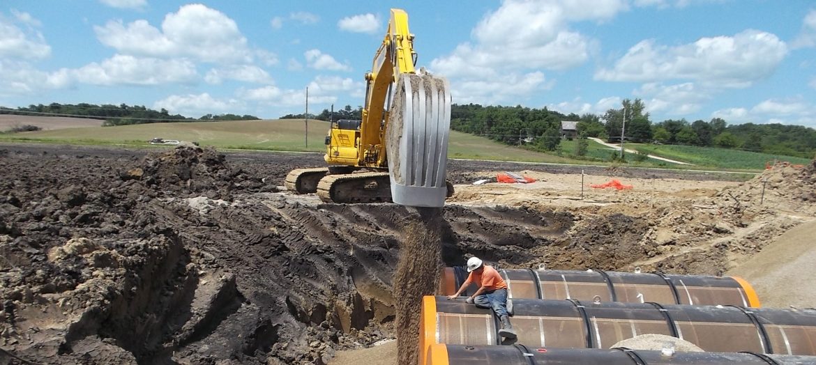 Acterra Group. An excavator fills in soil around tanks buried in the ground.