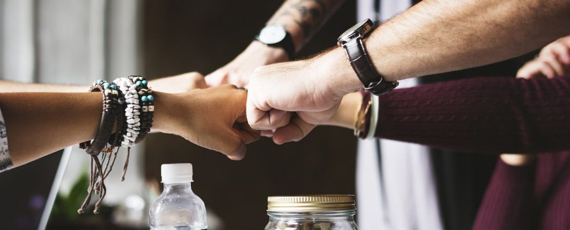 Best places to work. Photo shows multiple people putting their firsts together over a table.
