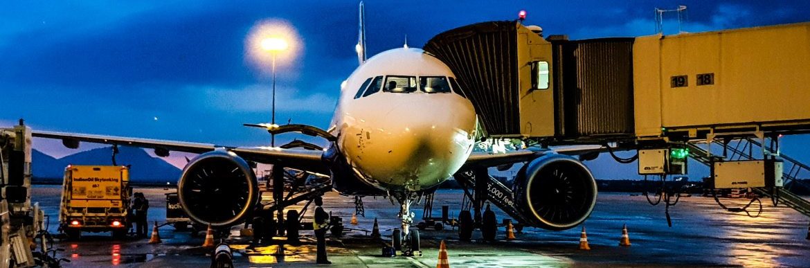 US Travel Report. A large jet parked at an airport terminal with walkway attached.