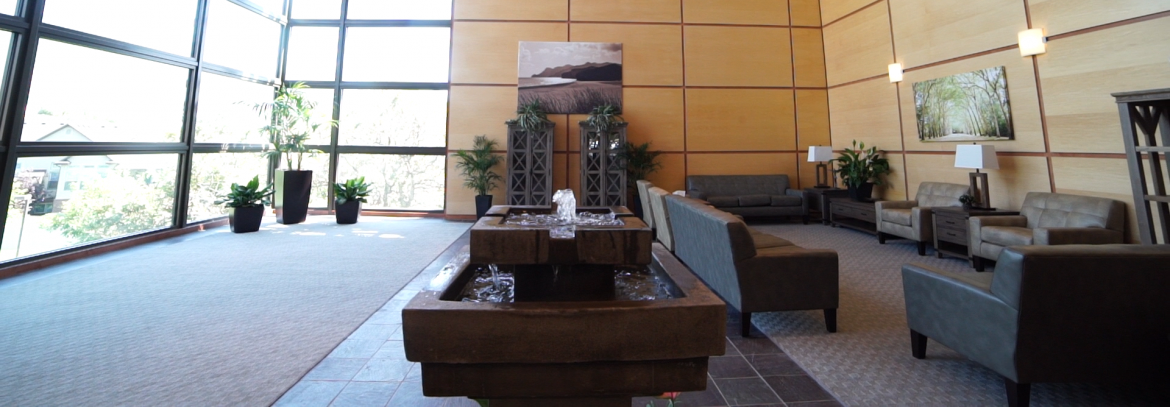 Brighton Recovery. A room with seats on the right, a fountain in the middle and windows/walls with a view of outside on the left.