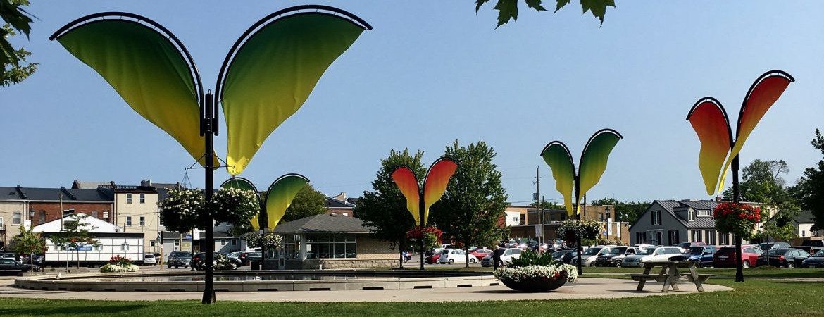 Cobourg Ontario, a view of a city park with wing like fixtures on poles, hanging plants underneath.