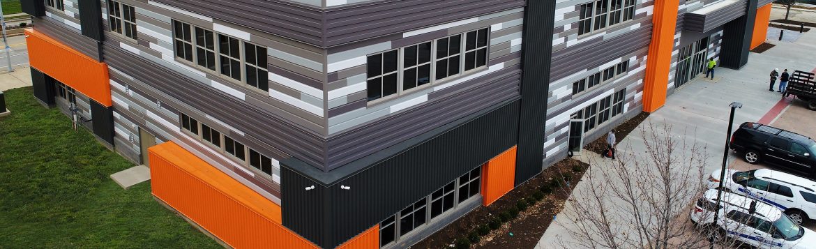 An aerial view of a modern looking metal building with cars parked to the right.