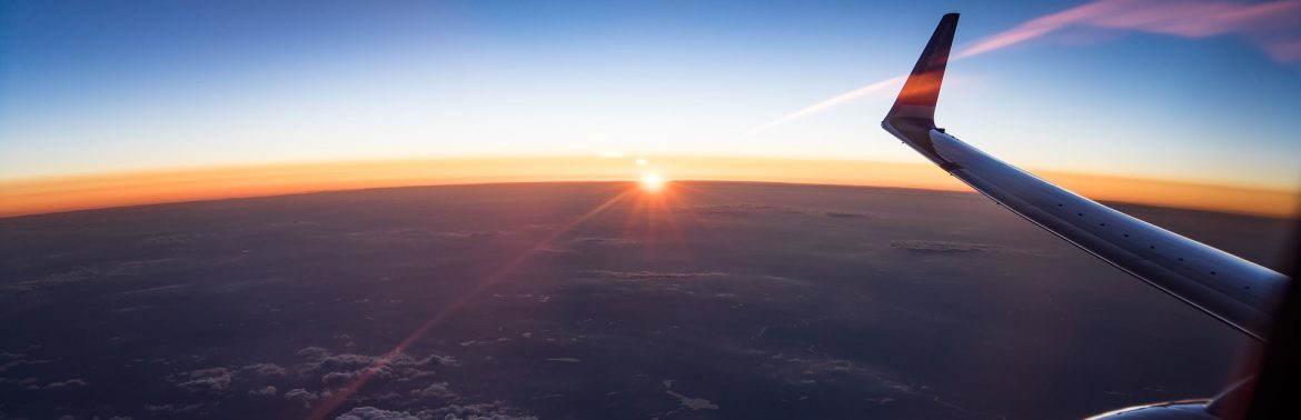 Knox County Regional Airport. A wing tip and part of the engine to a jet flying high up with the view of a sun setting on the horizon.
