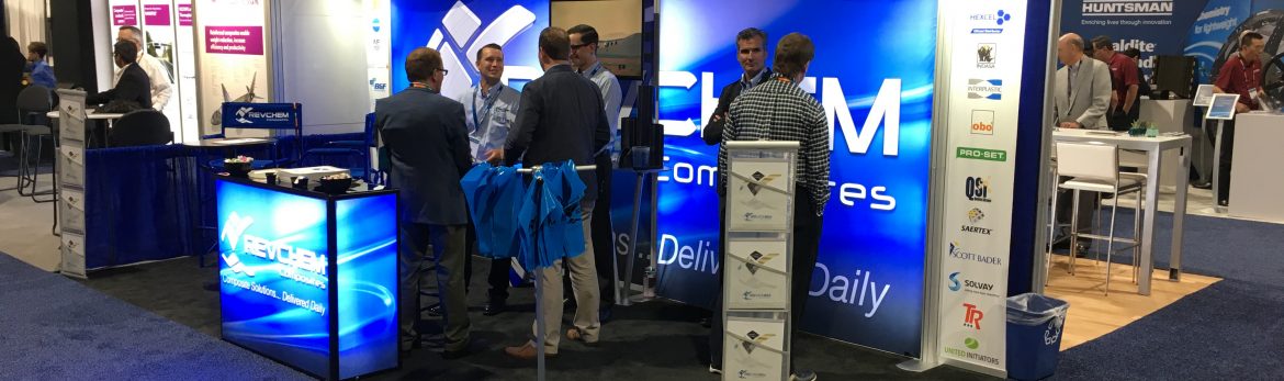A Revchem Composites display at a conference. Multiple people standing and talking.