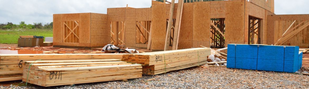 A new home construction site with wooden walls up and multiple stacks of lumber out front waiting to be used.