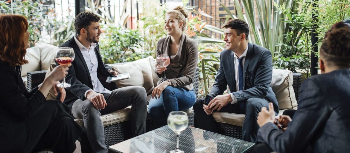 ActionCoach. A group of people sit around a small table, dressed nicely in suits drinking and talking.