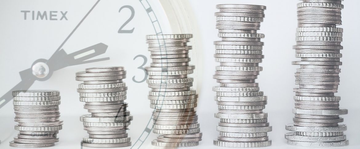 An image of 5 stacks of coins, increasing in height from left to right; image of a clock on the left of the image.