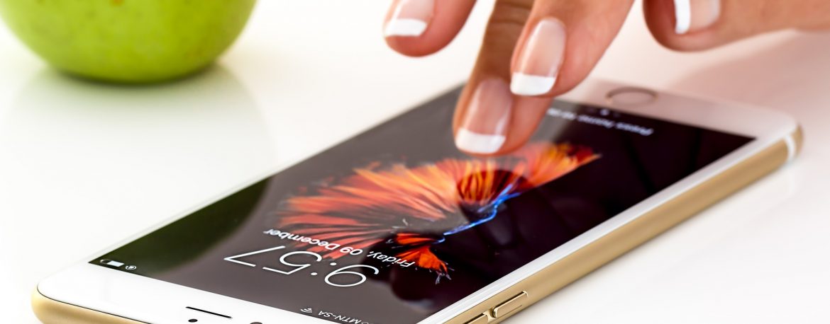 A woman tapping a mobile phone screen on a white table. Synchrony Study of consumer adoptions of retailer mobile apps.