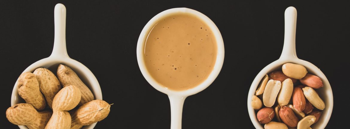 Peanuts in small bowls with handles. From left to right containing whole peanuts in the shell, peanut butter or paste, and shelled peanuts.