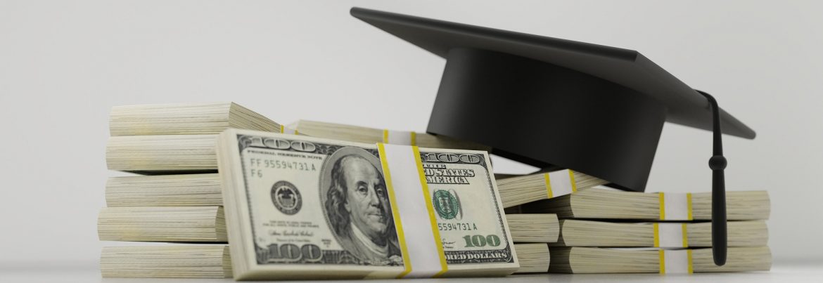 Bank wrapped hundred dollar bills stacked with a graduation cap on top.