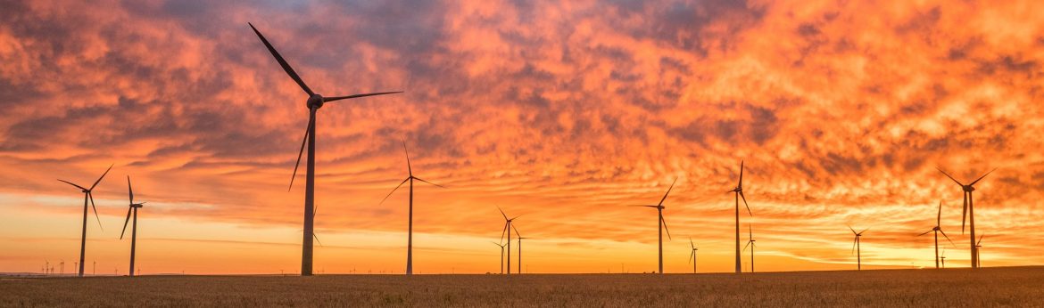 5 / energyby5 A field of wind turbines with an orange sky behind.