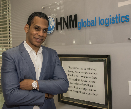 HNM Global Logistics CEO Tony McGee standing in front of a company sign and a framed quote.
