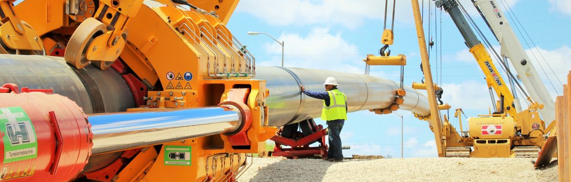 Laney Directional Drilling. A man at work with cranes holding up a pipe and a machine in the foreground.