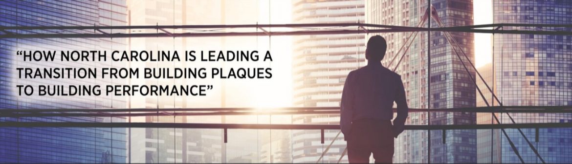 North Carolina Building Performance Association. A man standing looking out of a window at high rise buildings.