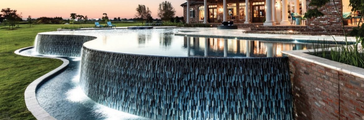 A great photo of a pool with water flowing over the edges of the pool with green grass near. The Association of Pool & Spa Professionals