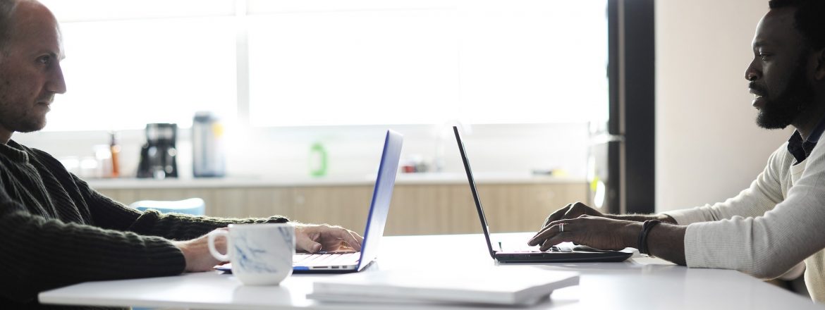 Two men at a table across from each other working on their laptops. Small Business Owners Look Beyond College for Training Opportunities