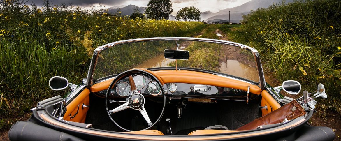 An older style convertible top car sitting on a dirt road in a field with trees and mountains on the horizon.