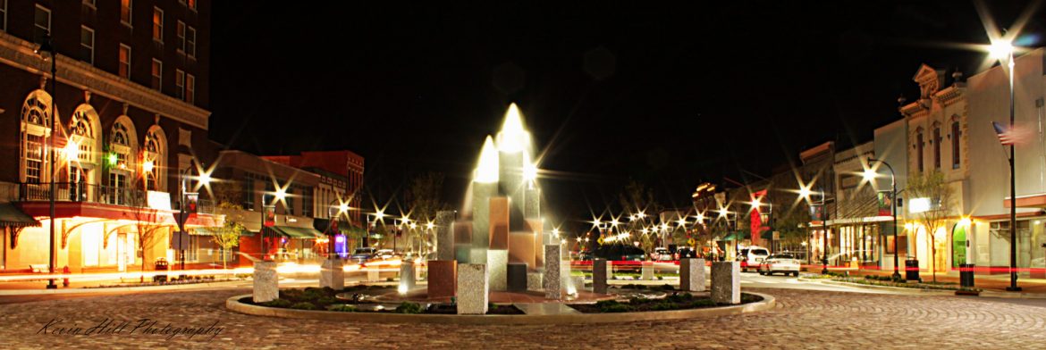 Goldsboro, North Carolina Center Street fountain in the median of a roadway at night with street lights on.