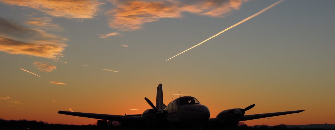 Warrenton-Fauquier Airport contrails and orange sky behind a plane silhouette on the runway.