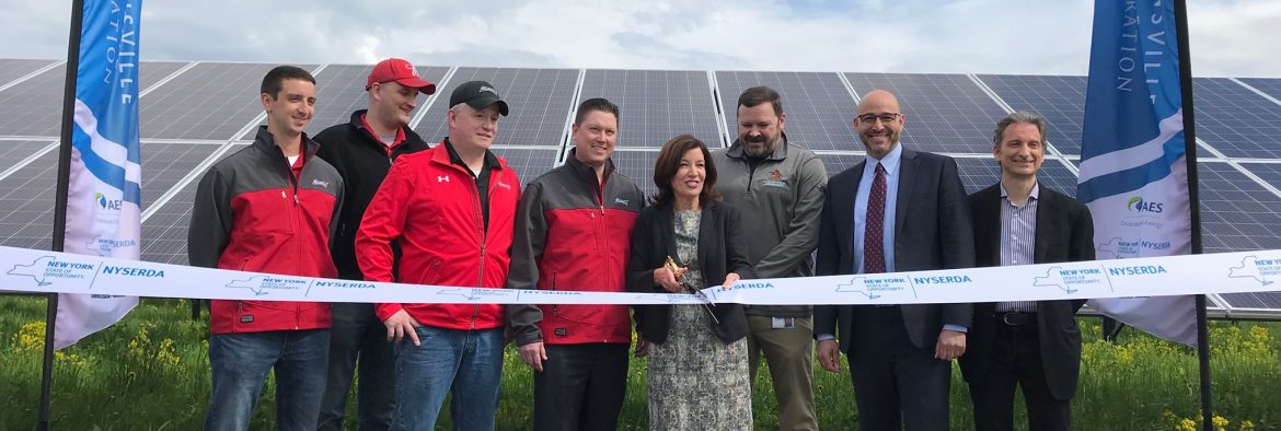 NYSERDA New York State Energy Research & Development Authority ribbon cutting ceremony with a solar panel in the background.
