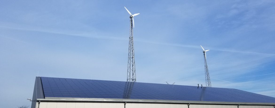 The Acterra Group example of work showing a roof covered in a solar panel with 2 wind turbines on towers visible behind.
