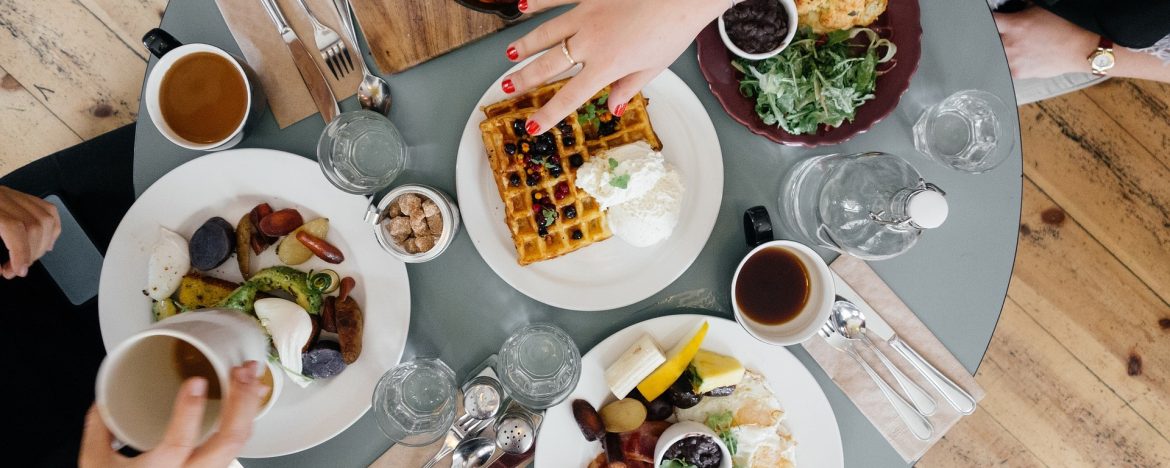 A table view from above with food and peoples hands in view reaching for drinks and food. OpenTable Reveals the 100 Best Restaurants in America for a Big Night Out