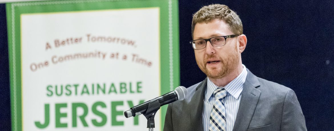Sustainable New Jersey Randall Solomon, Executive Director, speaking at a podium with a Sustainable Jersey poster behind him.