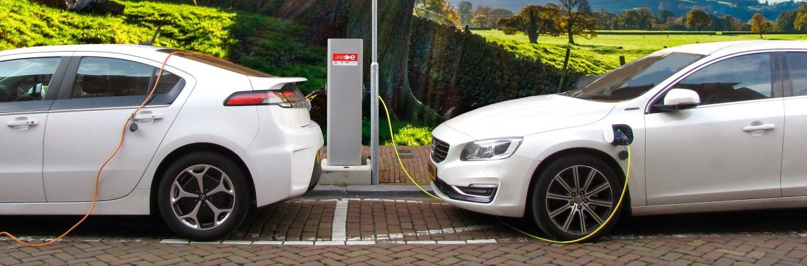 Two white cars plugged in to an EV charging station on a brick road with a tree behind them. Feature image for the Top Ten Sustainable Businesses in New Jersey.