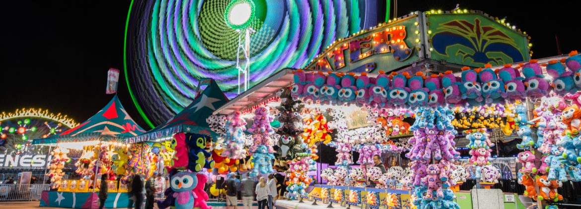 North Carolina State Fair colorful Ferris wheel in the background with games and people in the foreground.