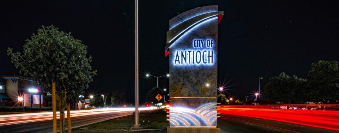 Antioch, California welcome sign at night with time laps headlights and taillights showing as streaks of light.