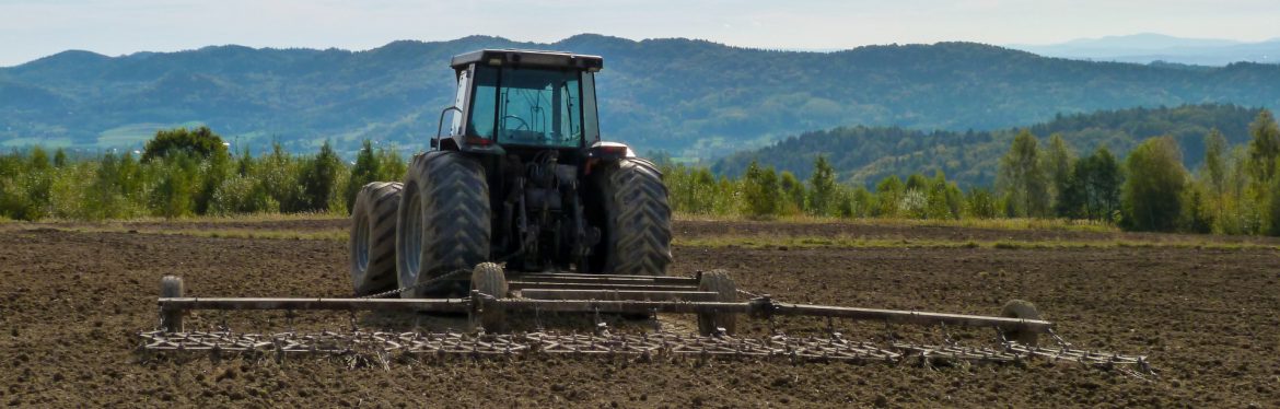 Walco Equipment Ltd. ; A tractor working a field with a hill / mountain in the background.
