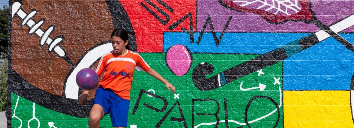 San Pablo, California wall art mural with a person practicing soccer in front on the sidewalk.