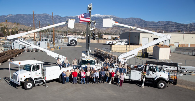 Banning, California Banning Electric Department vehicles and people posing for a group photo with an american flag on one of the vehicles booms in the air.