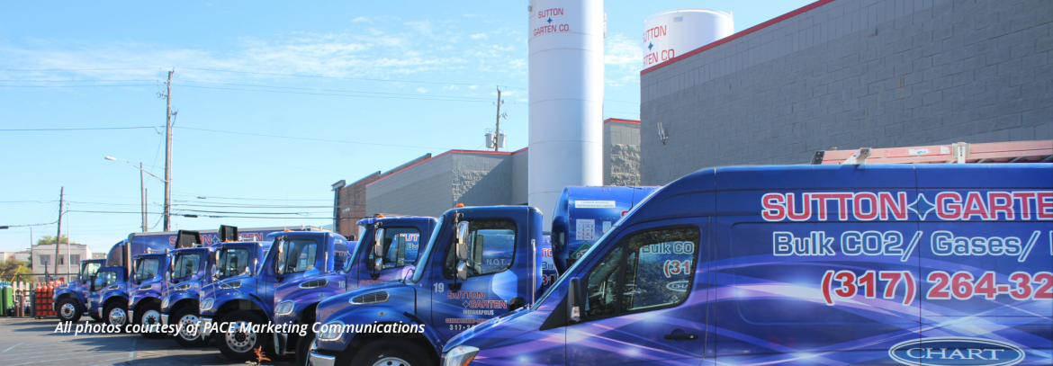 Sutton-Garten Co. lineup of vehicles at the building with blue sky and clouds in the background.