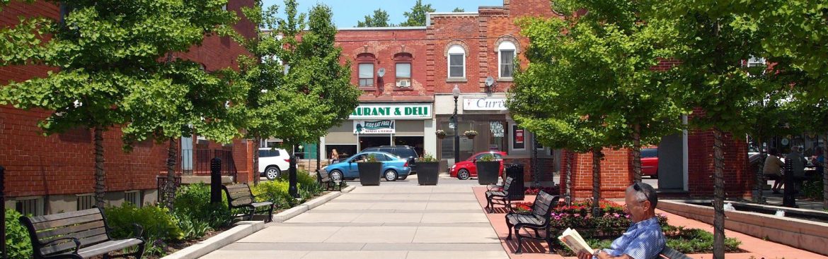 Whitchurch-Stouffville, Ontario public area with a man on a bench reading and a city street behind.