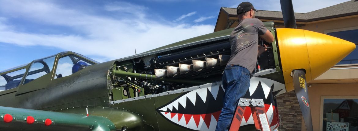 Yakima Air Terminal McAllister Field Wings of Freedom plane with teeth on the front with the engine compartment open and a man working on it.