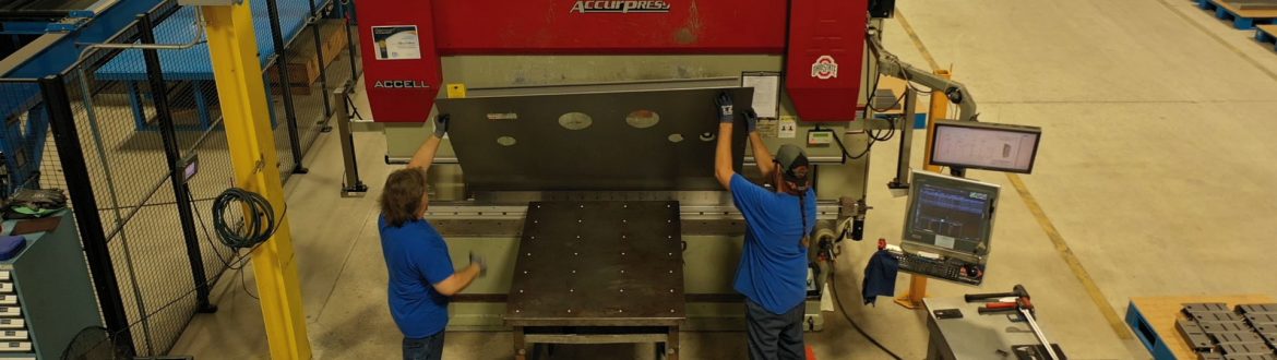 Earnest Products two people handling a piece of metal on a large machine press.