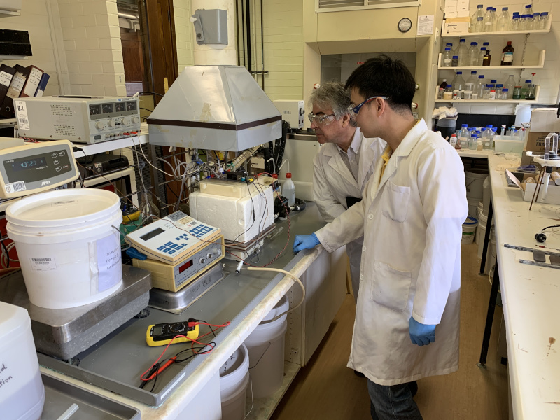 Element 25 Electrolyctic Manganese Metal testwork. Two men in a lab with shelves and equipment around them.