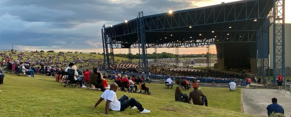 Ford Park event with people sitting on grass looking at a pavillion.