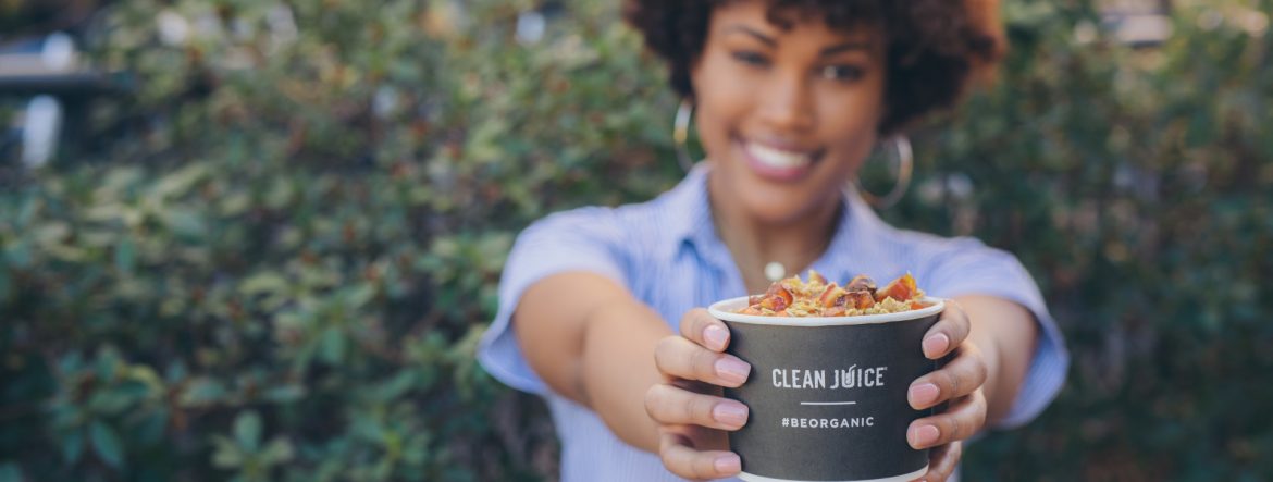 Clean Juice woman holding a cup of Clean Juice product with outstretched arms, focused on the cup.