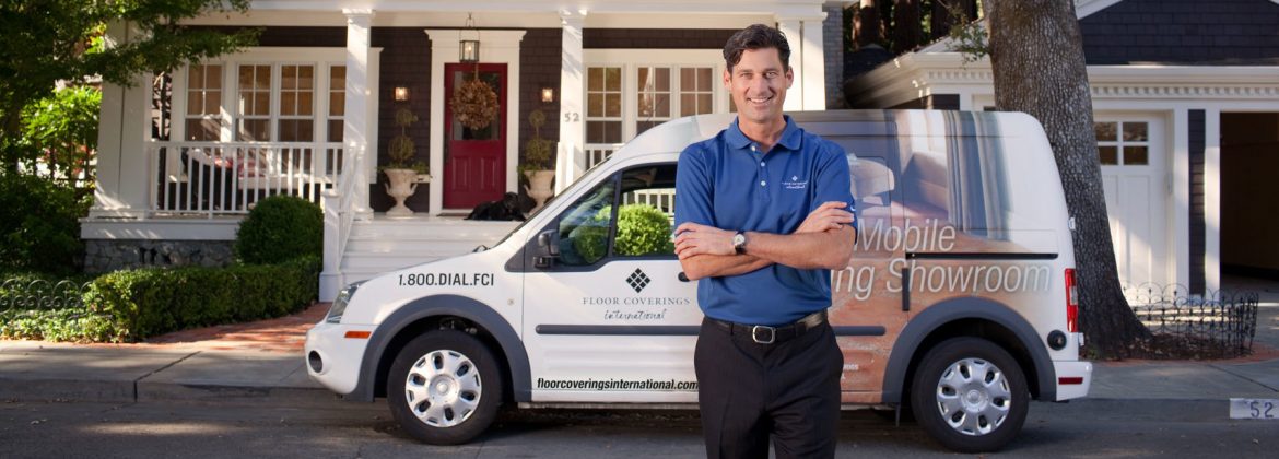 Floor Coverings International employee in front of a company vehicle and a house behind.