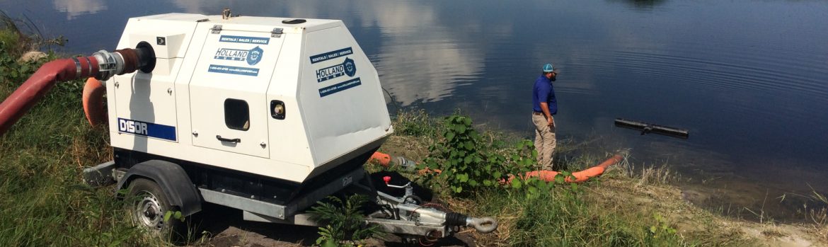 Holland Pump Company pump on the bank of a body of water and a worker down by the water.