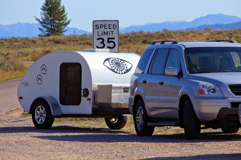 The Recreation Vehicle Industry Association RVIA teardrop camper on the side of a road behind car.